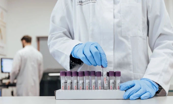 Person in a lab coat and gloves handling test tubes in a laboratory setting.