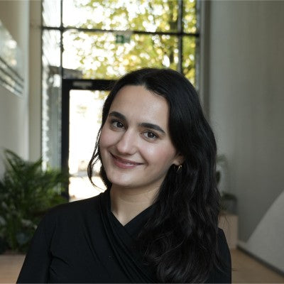 Woman with dark hair and a black outfit standing indoors with a blurred background