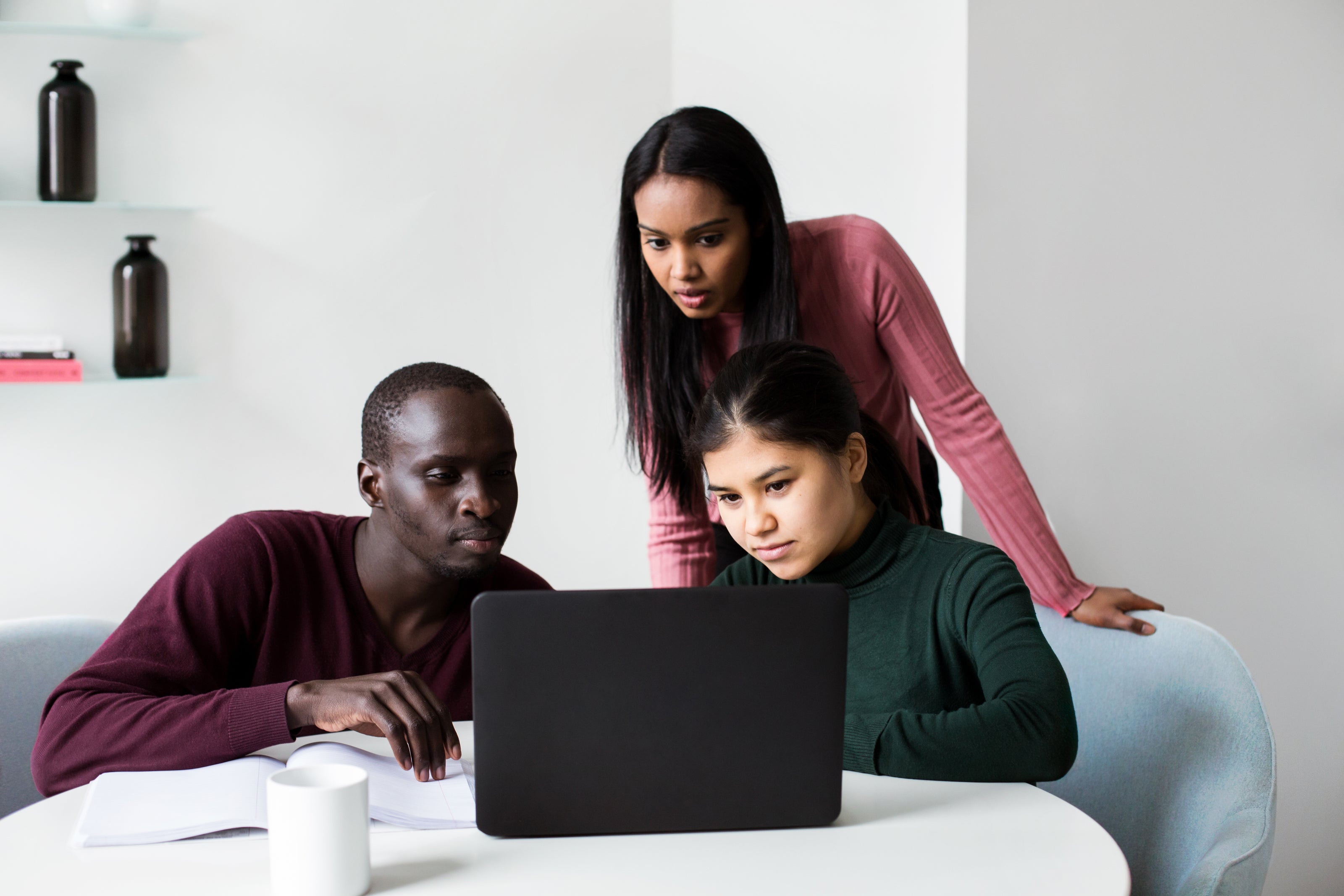 Three people looking at a laptop reading something.