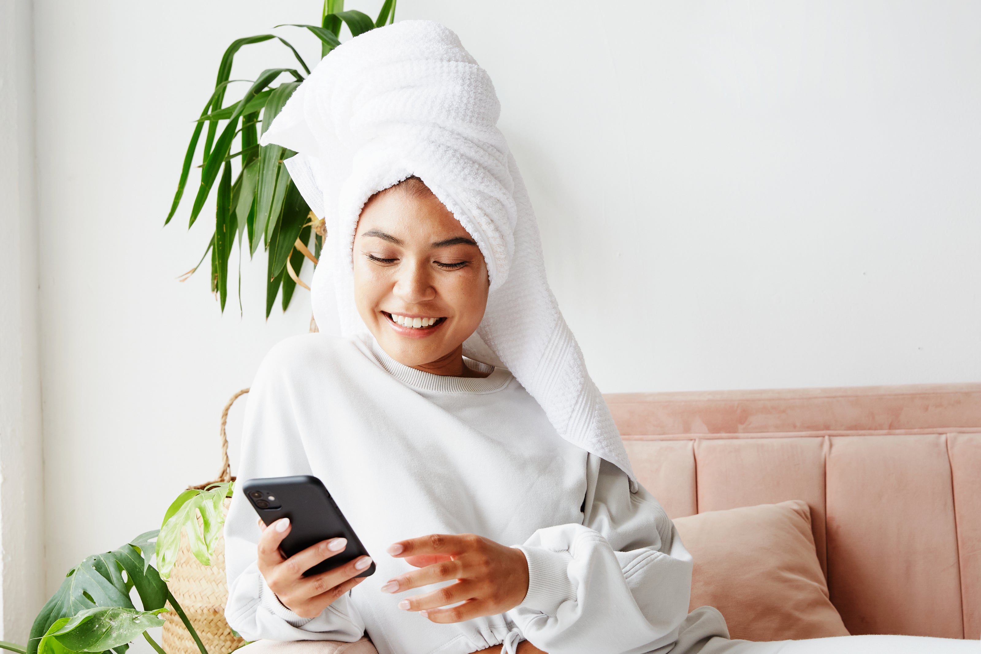 Young Asian woman looking at her phone smiling while sitting on her couch.