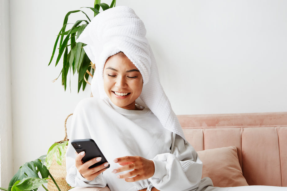 Woman with a towel wrapped around her head using a phone in a bright room checking her AMH results that just came in.
